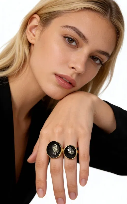 Ανακαλύψτε τη μαγεία του χειροποίητου γυναικείου δαχτυλιδιού με πυρίτη, ένα μοναδικό κόσμημα που συνδυάζει τη δύναμη των φυσικών πετρών με τη σύγχρονη αισθητική. Σχεδιασμένο από την Ελληνίδα Σχεδιάστρια Κοσμημάτων Αικατερίνη Χαλκιαδάκη, αυτό το εντυπωσιακό δαχτυλίδι αποτελεί την τέλεια επιλογή για γυναίκες που αναζητούν statement κοσμήματα με χαρακτήρα.
Η ωοειδής σιλουέτα του δαχτυλιδιού περιβάλλεται από χρυσαφί ορείχαλκο, ενώ στο κέντρο κυριαρχεί η μαύρη πατίνα που φιλοξενεί έναν φυσικό σιδηροπυρίτη. Ο πυρίτης προσφέρει μεταλλικές ανταύγειες που δημιουργούν έναν μαγευτικό οπτικό διάλογο με το μαύρο φόντο.
Το μεγάλο μέγεθος του δαχτυλιδιού το καθιστά ιδανικό για όσες προτιμούν εντυπωσιακά κοσμήματα που ξεχωρίζουν. Η χειροποίητη κατασκευή εγγυάται την μοναδικότητα κάθε κομματιού, καθιστώντας το ένα πραγματικό έργο τέχνης.