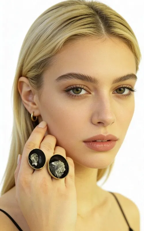 , Ανακαλύψτε την τέλεια ισορροπία μεταξύ δύναμης και κομψότητας με αυτό το μεγάλο εντυπωσιακό γυναικείο δαχτυλίδι με διπλό πυρίτη, σχεδιασμένο από την Αικατερίνη Χαλκιαδάκη. Το μοναδικό χειροποίητο δαχτυλίδι συνδυάζει δύο φυσικούς κρυστάλλους σιδηροπυρίτη σε μια εκπληκτική σύνθεση που κεντρίζει τα βλέμματα.
Η μαύρη πατίνα δημιουργεί εντυπωσιακή αντίθεση με τα χρυσαφί κρύσταλλα του πυρίτη, ενώ ο ορείχαλκος προσδίδει θερμότητα και διαρκότητα στο κόσμημα. Η ανοιχτή δομή του δαχτυλιδιού επιτρέπει την άνετη εφαρμογή σε διάφορα μεγέθη δακτύλου, ενώ οι δύο ωοειδείς πέτρες πυρίτη σε διαφορετικά μεγέθη δημιουργούν δυναμική σύνθεση.
Ο σιδηροπυρίτης θεωρείται πέτρα προστασίας και δύναμης, ιδανική για γυναίκες που θέλουν να εκφράσουν την προσωπικότητά τους με στυλ. Το statement δαχτυλίδι συνδυάζεται τέλεια με casual και επίσημα outfits, προσδίδοντας μοναδικό χαρακτήρα σε κάθε εμφάνιση.
