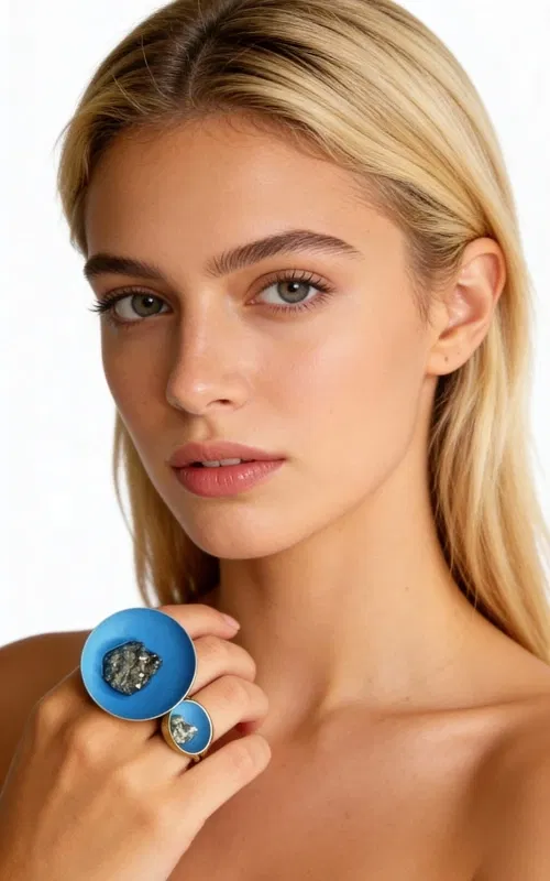 , Ένα εντυπωσιακό statement δαχτυλίδι που συνδυάζει τη φυσική ομορφιά του σιδηροπυρίτη με το έντονο γαλάζιο χρώμα κιμωλίας, σχεδιασμένο από την Ελληνίδα Σχεδιάστρια Κοσμημάτων Αικατερίνη Χαλκιαδάκη. Το μεγάλο χειροποίητο δαχτυλίδι διαθέτει δύο διαφορετικές σφαίρες που δημιουργούν μια μοντέρνα και asymmetric αισθητική.
Η μεγαλύτερη σφαίρα φιλοξενεί έναν μεγάλο κρύσταλλο σιδηροπυρίτη, ενώ η μικρότερη διακοσμείται με έναν πιο μικρό κρύσταλλο, δημιουργώντας μια εντυπωσιακή σύνθεση που τραβάει τα βλέμματα. Το χρώμα της κιμωλίας σε γαλάζια απόχρωση προσδίδει μια μοναδική vintage αύρα, ενώ ο ορείχαλκος εξασφαλίζει ανθεκτικότητα και διάρκεια.
Αυτό το χειροποίητο γυναικείο δαχτυλίδι είναι ιδανικό για όσες αγαπούν τα μεγάλα κοσμήματα που κάνουν statement. Συνδυάζεται τέλεια με casual και bohemian looks, προσδίδοντας έναν εκλεκτικό χαρακτήρα σε κάθε εμφάνιση.