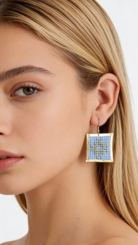 , Τα statement σκουλαρίκια με κεντητά γεωμετρικά σχέδια σε γαλάζιο χρώμα θα γίνουν το αγαπημένο σας αξεσουάρ για κάθε ιδιαίτερη περίσταση. Σχεδιασμένα από την Ελληνίδα Σχεδιάστρια Κοσμημάτων Αικατερίνη Χαλκιαδάκη, αυτά τα εντυπωσιακά χειροποίητα σκουλαρίκια συνδυάζουν την παραδοσιακή τέχνη του κεντήματος με σύγχρονο design.
Η χρυσοκλωστή σε απαλό γαλάζιο χρώμα δημιουργεί ένα μοναδικό γεωμετρικό μοτίβο που προσθέτει κομψότητα και στυλ σε κάθε εμφάνιση. Τα κεντητά σκουλαρίκια έχουν τετράγωνο σχήμα και μεσαίο μέγεθος, ιδανικό για να κάνουν statement χωρίς να είναι υπερβολικά βαριά. Η λεπτομερής χειροτεχνία και το folklore design τους κάνουν ιδιαίτερα για βραδινές εξόδους, ειδικές εκδηλώσεις ή ακόμα και για γαμήλιες εμφανίσεις. Συντηρήστε τα σκουλαρίκια σας αποθηκεύοντάς τα σε στεγνό μέρος και αποφεύγοντας την επαφή με νερό ή χημικά προϊόντα για να διατηρήσουν το χρώμα τους.