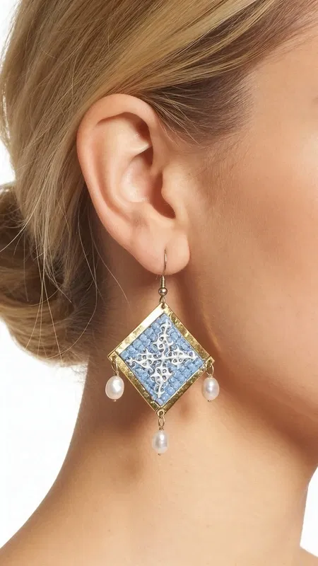 , Τα statement κεντητά σκουλαρίκια σε γαλάζιο χρώμα με γεωμετρικά σχέδια από χρυσοκλωστή αποτελούν το ιδανικό χειροποίητο κόσμημα για να αναδείξετε τη μοναδικότητά σας. Αυτά τα εντυπωσιακά κρεμαστά σκουλαρίκια, σχεδιασμένα από την Ελληνίδα Σχεδιάστρια Κοσμημάτων Αικατερίνη Χαλκιαδάκη, συνδυάζουν την παραδοσιακή τέχνη του κεντήματος με μοντέρνα αισθητική.
Η γαλάζια απόχρωση σε συνδυασμό με τη χρυσοκλωστή δημιουργεί μια εκλεπτυσμένη αντίθεση που προσελκύει τα βλέμματα. Τα γεωμετρικά σχέδια προσδίδουν σύγχρονο χαρακτήρα, ενώ οι λεπτές πέρλες που κρέμονται από τη βάση των σκουλαρικιών προσθέτουν κίνηση και θηλυκότητα. Το folklore design τους τα καθιστά ιδανικά για ιδιαίτερες στιγμές, από νυφικές εμφανίσεις έως κοκτέιλ παρτυ. Ιδανικά σκουλαρίκαι για γάμους, βαπτίσεις και ιδιαίτερες εκδηλώσεις. Συντηρείστε τα με προσοχή, αποφεύγοντας την επαφή με νερό και αρώματα για μεγαλύτερη διάρκεια ζωής.