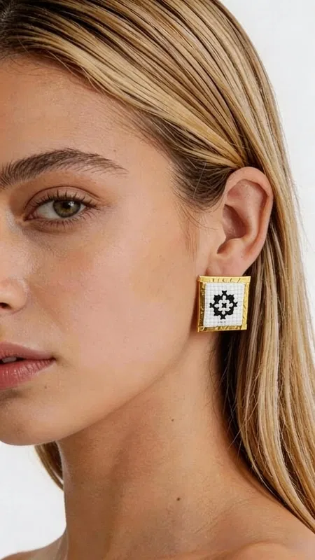 , Τα κεντητά σκουλαρίκια statement με γεωμετρικά σχέδια από χρυσοκλωστή σε άσπρο αποτελούν την τέλεια επιλογή για τη γυναίκα που αναζητά εντυπωσιακά και μοντέρνα κοσμήματα. Σχεδιασμένα από την Ελληνίδα Σχεδιάστρια Κοσμημάτων Αικατερίνη Χαλκιαδάκη, συνδυάζουν την παραδοσιακή τέχνη του κεντήματος με σύγχρονη αισθητική. Κάθε σκουλαρίκι διαθέτει τετράγωνη φόρμα με εκλεπτυσμένο γεωμετρικό μοτίβο κεντημένο με χρυσοκλωστή σε λευκή βάση. Το folklore design δημιουργεί μια μοναδική αντίθεση που προσδίδει κομψότητα και χαρακτήρα σε κάθε εμφάνιση. Τα χειροποίητα σκουλαρίκια είναι ιδανικά για γάμο, ειδικές εκδηλώσεις ή ως καθημερινό statement κόσμημα. Η υψηλή ποιότητα κατασκευής και τα επιλεγμένα υλικά εγγυώνται ανθεκτικότητα και άνεση στη χρήση. Το ελαφρύ τους βάρος τα καθιστά κατάλληλα για όλη τη μέρα, ενώ το μέγεθός τους προσδίδει τη σωστή δόση glamour χωρίς υπερβολή. Υλικό: Ορείχαλκος, Ύφασμα Φροντίστε τα σκουλαρίκια σας αποφεύγοντας την επαφή με νερό και αρώματα. Φυλάσσετε τα σε στεγνό μέρος για να διατηρήσουν τη λάμψη τους.