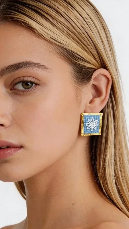 Ανακαλύψτε τη μαγεία των κεντητών statement σκουλαρικιών με γεωμετρικά σχέδια από χρυσοκλωστή σε εντυπωσιακό γαλάζιο χρώμα. Αυτά τα εξαιρετικά χειροποίητα σκουλαρίκια, σχεδιασμένα από την Ελληνίδα Σχεδιάστρια Κοσμημάτων Αικατερίνη Χαλκιαδάκη, συνδυάζουν την παραδοσιακή τέχνη του κεντήματος με σύγχρονη αισθητική. Το κάθε σκουλαρίκι διακοσμείται με περίτεχνα γεωμετρικά μοτίβα που κεντήθηκαν με χρυσή κλωστή σε έντονο γαλάζιο υπόβαθρο, δημιουργώντας ένα μοναδικό κέντημα που θυμίζει την ελληνική παραδοσιακή τέχνη. Η τετράγωνη φόρμα και το χρυσό περίγραμμα προσθέτουν μία κομψή νότα που κάνει αυτά τα εντυπωσιακά σκουλαρίκια ιδανικά για κάθε περίσταση. Τα statement σκουλαρίκια αυτά είναι τέλεια για να συμπληρώσουν ένα νυφικό look, έναν επίσημο εορταστικό εμφανισμό ή ακόμα και ένα casual σύνολο που θέλετε να ξεχωρίσει. Η υψηλή ποιότητα κατασκευής και το πρωτότυπο σχέδιο τα καθιστούν ένα μοναδικό κομμάτι που θα απογειώσει το στυλ σας. Υλικό: Ορείχαλκος, Ύφασμα Φροντίστε τα με προσοχή, αποφεύγοντας την επαφή με νερό και αρώματα για τη διατήρηση των χρωμάτων.