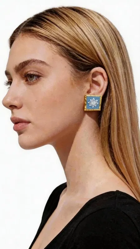 , Ανακαλύψτε τη μαγεία των κεντητών statement σκουλαρικιών με γεωμετρικά σχέδια από χρυσοκλωστή σε εντυπωσιακό γαλάζιο χρώμα. Αυτά τα εξαιρετικά χειροποίητα σκουλαρίκια, σχεδιασμένα από την Ελληνίδα Σχεδιάστρια Κοσμημάτων Αικατερίνη Χαλκιαδάκη, συνδυάζουν την παραδοσιακή τέχνη του κεντήματος με σύγχρονη αισθητική. Το κάθε σκουλαρίκι διακοσμείται με περίτεχνα γεωμετρικά μοτίβα που κεντήθηκαν με χρυσή κλωστή σε έντονο γαλάζιο υπόβαθρο, δημιουργώντας ένα μοναδικό κέντημα που θυμίζει την ελληνική παραδοσιακή τέχνη. Η τετράγωνη φόρμα και το χρυσό περίγραμμα προσθέτουν μία κομψή νότα που κάνει αυτά τα εντυπωσιακά σκουλαρίκια ιδανικά για κάθε περίσταση. Τα statement σκουλαρίκια αυτά είναι τέλεια για να συμπληρώσουν ένα νυφικό look, έναν επίσημο εορταστικό εμφανισμό ή ακόμα και ένα casual σύνολο που θέλετε να ξεχωρίσει. Η υψηλή ποιότητα κατασκευής και το πρωτότυπο σχέδιο τα καθιστούν ένα μοναδικό κομμάτι που θα απογειώσει το στυλ σας. Υλικό: Ορείχαλκος, Ύφασμα Φροντίστε τα με προσοχή, αποφεύγοντας την επαφή με νερό και αρώματα για τη διατήρηση των χρωμάτων.