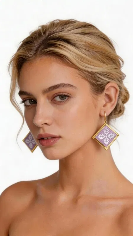 Τα statement κεντητά σκουλαρίκια σε λιλά απόχρωση με γεωμετρικά σχέδια από χρυσοκλωστή είναι η τέλεια επιλογή για να προσθέσετε μια πινελιά κομψότητας και πρωτοτυπίας στην εμφάνισή σας. Σχεδιασμένα από την Ελληνίδα Σχεδιάστρια Κοσμημάτων Αικατερίνη Χαλκιαδάκη, αυτά τα χειροποίητα σκουλαρίκια συνδυάζουν την παραδοσιακή τεχνική του κεντήματος με σύγχρονο design. Η τετράγωνη γεωμετρική φόρμα τους διακοσμείται με περίτεχνα κεντημένα μοτίβα σε μαλακή λιλά απόχρωση, ενώ το χρυσό περίγραμμα προσδίδει μια πολυτελή πινελιά. Το folklore design με τα λεπτομερή γεωμετρικά σχέδια δημιουργεί ένα μοναδικό κόσμημα που ξεχωρίζει και συμπληρώνει τόσο casual όσο και επίσημα looks. Ιδανικά για γυναίκες που αγαπούν τα εντυπωσιακά αξεσουάρ, αυτά τα σκουλαρίκια είναι τέλεια για ειδικές περιστάσεις, γάμους ή για να προσθέσουν χρώμα στην καθημερινότητά σας. Υλικό: Ορείχαλκος, Ύφασμα Για τη φροντίδα τους, φυλάσσετε τα σκουλαρίκια σε στεγνό μέρος και αποφεύγετε την επαφή με νερό και χημικά.