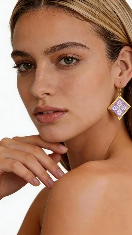 , Τα statement κεντητά σκουλαρίκια σε λιλά απόχρωση με γεωμετρικά σχέδια από χρυσοκλωστή είναι η τέλεια επιλογή για να προσθέσετε μια πινελιά κομψότητας και πρωτοτυπίας στην εμφάνισή σας. Σχεδιασμένα από την Ελληνίδα Σχεδιάστρια Κοσμημάτων Αικατερίνη Χαλκιαδάκη, αυτά τα χειροποίητα σκουλαρίκια συνδυάζουν την παραδοσιακή τεχνική του κεντήματος με σύγχρονο design. Η τετράγωνη γεωμετρική φόρμα τους διακοσμείται με περίτεχνα κεντημένα μοτίβα σε μαλακή λιλά απόχρωση, ενώ το χρυσό περίγραμμα προσδίδει μια πολυτελή πινελιά. Το folklore design με τα λεπτομερή γεωμετρικά σχέδια δημιουργεί ένα μοναδικό κόσμημα που ξεχωρίζει και συμπληρώνει τόσο casual όσο και επίσημα looks. Ιδανικά για γυναίκες που αγαπούν τα εντυπωσιακά αξεσουάρ, αυτά τα σκουλαρίκια είναι τέλεια για ειδικές περιστάσεις, γάμους ή για να προσθέσουν χρώμα στην καθημερινότητά σας. Υλικό: Ορείχαλκος, Ύφασμα Για τη φροντίδα τους, φυλάσσετε τα σκουλαρίκια σε στεγνό μέρος και αποφεύγετε την επαφή με νερό και χημικά.