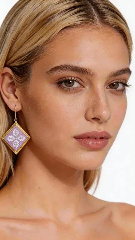 , Τα statement κεντητά σκουλαρίκια σε λιλά απόχρωση με γεωμετρικά σχέδια από χρυσοκλωστή είναι η τέλεια επιλογή για να προσθέσετε μια πινελιά κομψότητας και πρωτοτυπίας στην εμφάνισή σας. Σχεδιασμένα από την Ελληνίδα Σχεδιάστρια Κοσμημάτων Αικατερίνη Χαλκιαδάκη, αυτά τα χειροποίητα σκουλαρίκια συνδυάζουν την παραδοσιακή τεχνική του κεντήματος με σύγχρονο design. Η τετράγωνη γεωμετρική φόρμα τους διακοσμείται με περίτεχνα κεντημένα μοτίβα σε μαλακή λιλά απόχρωση, ενώ το χρυσό περίγραμμα προσδίδει μια πολυτελή πινελιά. Το folklore design με τα λεπτομερή γεωμετρικά σχέδια δημιουργεί ένα μοναδικό κόσμημα που ξεχωρίζει και συμπληρώνει τόσο casual όσο και επίσημα looks. Ιδανικά για γυναίκες που αγαπούν τα εντυπωσιακά αξεσουάρ, αυτά τα σκουλαρίκια είναι τέλεια για ειδικές περιστάσεις, γάμους ή για να προσθέσουν χρώμα στην καθημερινότητά σας. Υλικό: Ορείχαλκος, Ύφασμα Για τη φροντίδα τους, φυλάσσετε τα σκουλαρίκια σε στεγνό μέρος και αποφεύγετε την επαφή με νερό και χημικά.