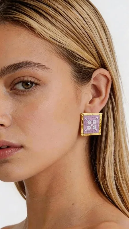 , Τα κεντητά statement σκουλαρίκια με γεωμετρικά σχέδια σε λιλά απόχρωση θα γίνουν το αγαπημένο σας αξεσουάρ για κάθε ιδιαίτερη περίσταση. Σχεδιασμένα από την Ελληνίδα Σχεδιάστρια Κοσμημάτων Αικατερίνη Χαλκιαδάκη, αυτά τα εντυπωσιακά χειροποίητα σκουλαρίκια συνδυάζουν την παραδοσιακή τέχνη του κεντήματος με σύγχρονο design. Η τετράγωνη φόρμα με τα περίτεχνα γεωμετρικά μοτίβα δημιουργεί ένα μοναδικό οπτικό αποτέλεσμα, ενώ η χρυσοκλωστή προσδίδει λάμψη και κομψότητα. Το ρομαντικό λιλά χρώμα αναδεικνύει την θηλυκότητα και προσφέρει ευελιξία στον συνδυασμό με διάφορα outfits. Αυτά τα μοντέρνα κεντητά σκουλαρίκια είναι ιδανικά για γάμους, βραδινές εξόδους αλλά και για να αναβαθμίσετε την καθημερινή σας εμφάνιση. Η χειροποίητη κατασκευή εγγυάται τη μοναδικότητα και την ποιότητα κάθε κομματιού. Υλικό: Ορείχαλκος, Ύφασμα **Φροντίδα:** Φυλάσσετε τα σκουλαρίκια σε στεγνό μέρος και αποφεύγετε την επαφή με νερό και καλλυντικά για να διατηρήσετε τη λάμψη της χρυσοκλωστής.