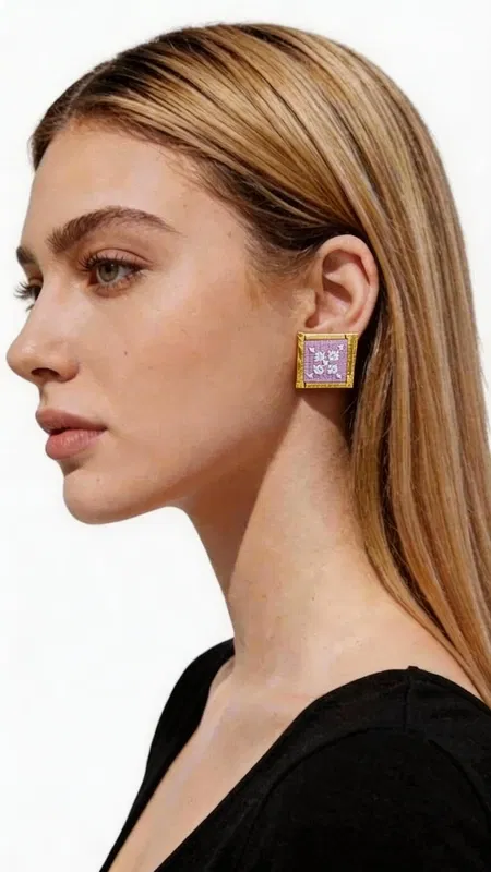 , Τα κεντητά statement σκουλαρίκια με γεωμετρικά σχέδια σε λιλά απόχρωση θα γίνουν το αγαπημένο σας αξεσουάρ για κάθε ιδιαίτερη περίσταση. Σχεδιασμένα από την Ελληνίδα Σχεδιάστρια Κοσμημάτων Αικατερίνη Χαλκιαδάκη, αυτά τα εντυπωσιακά χειροποίητα σκουλαρίκια συνδυάζουν την παραδοσιακή τέχνη του κεντήματος με σύγχρονο design. Η τετράγωνη φόρμα με τα περίτεχνα γεωμετρικά μοτίβα δημιουργεί ένα μοναδικό οπτικό αποτέλεσμα, ενώ η χρυσοκλωστή προσδίδει λάμψη και κομψότητα. Το ρομαντικό λιλά χρώμα αναδεικνύει την θηλυκότητα και προσφέρει ευελιξία στον συνδυασμό με διάφορα outfits. Αυτά τα μοντέρνα κεντητά σκουλαρίκια είναι ιδανικά για γάμους, βραδινές εξόδους αλλά και για να αναβαθμίσετε την καθημερινή σας εμφάνιση. Η χειροποίητη κατασκευή εγγυάται τη μοναδικότητα και την ποιότητα κάθε κομματιού. Υλικό: Ορείχαλκος, Ύφασμα **Φροντίδα:** Φυλάσσετε τα σκουλαρίκια σε στεγνό μέρος και αποφεύγετε την επαφή με νερό και καλλυντικά για να διατηρήσετε τη λάμψη της χρυσοκλωστής.