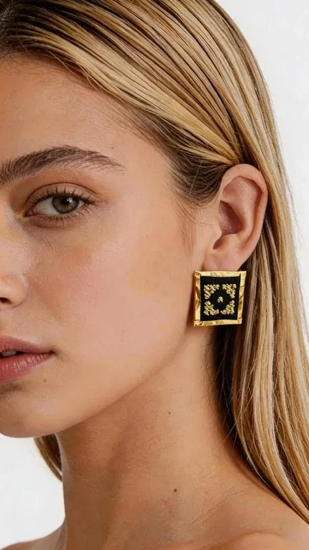 Ξεχωρίστε με αυτά τα εντυπωσιακά statement κεντητά σκουλαρίκια που συνδυάζουν την παραδοσιακή ελληνική τέχνη του κεντήματος με σύγχρονο γεωμετρικό design. Σχεδιασμένα από την Ελληνίδα Σχεδιάστρια Κοσμημάτων Αικατερίνη Χαλκιαδάκη, αυτά τα μοναδικά χειροποίητα σκουλαρίκια φέρουν έναν πλούσιο χρυσόκλωστο κεντητό σχεδιασμό πάνω σε κομψό μαύρο φόντο. Κάθε σκουλαρίκι αποτελεί ένα μικρό έργο τέχνης με περίπλοκα γεωμετρικά μοτίβα που δημιουργούν μια εκπληκτική οπτική αίσθηση. Η χρυσή κλωστή λάμπει υπέροχα πάνω στη μαύρη βάση, προσφέροντας έναν εντυπωσιακό συνδυασμό που ταιριάζει τόσο σε καθημερινές όσο και σε επίσημες εμφανίσεις. Αυτά τα μοντέρνα κρεμαστά σκουλαρίκια είναι ιδανικά για γυναίκες που αγαπούν τα πρωτότυπα κοσμήματα με ελληνικό χαρακτήρα. Το τετράγωνο σχήμα τους προσφέρει μια σύγχρονη αισθητική, ενώ η κεντητή λεπτομέρεια φέρνει την παράδοση στο προσκήνιο. Υλικό: Ορείχαλκος, Ύφασμα Φροντίστε τα σκουλαρίκια σας αποθηκεύοντάς τα σε στεγνό μέρος και αποφεύγοντας την επαφή με υγρασία και χημικά προϊόντα.