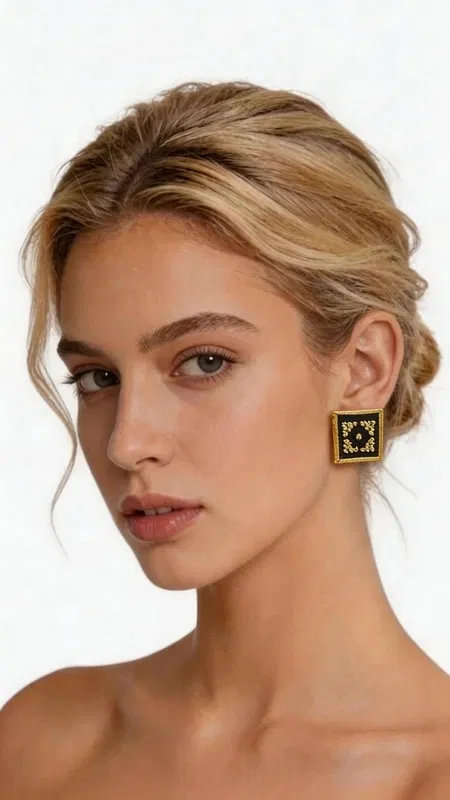 , Ξεχωρίστε με αυτά τα εντυπωσιακά statement κεντητά σκουλαρίκια που συνδυάζουν την παραδοσιακή ελληνική τέχνη του κεντήματος με σύγχρονο γεωμετρικό design. Σχεδιασμένα από την Ελληνίδα Σχεδιάστρια Κοσμημάτων Αικατερίνη Χαλκιαδάκη, αυτά τα μοναδικά χειροποίητα σκουλαρίκια φέρουν έναν πλούσιο χρυσόκλωστο κεντητό σχεδιασμό πάνω σε κομψό μαύρο φόντο. Κάθε σκουλαρίκι αποτελεί ένα μικρό έργο τέχνης με περίπλοκα γεωμετρικά μοτίβα που δημιουργούν μια εκπληκτική οπτική αίσθηση. Η χρυσή κλωστή λάμπει υπέροχα πάνω στη μαύρη βάση, προσφέροντας έναν εντυπωσιακό συνδυασμό που ταιριάζει τόσο σε καθημερινές όσο και σε επίσημες εμφανίσεις. Αυτά τα μοντέρνα κρεμαστά σκουλαρίκια είναι ιδανικά για γυναίκες που αγαπούν τα πρωτότυπα κοσμήματα με ελληνικό χαρακτήρα. Το τετράγωνο σχήμα τους προσφέρει μια σύγχρονη αισθητική, ενώ η κεντητή λεπτομέρεια φέρνει την παράδοση στο προσκήνιο. Υλικό: Ορείχαλκος, Ύφασμα Φροντίστε τα σκουλαρίκια σας αποθηκεύοντάς τα σε στεγνό μέρος και αποφεύγοντας την επαφή με υγρασία και χημικά προϊόντα.