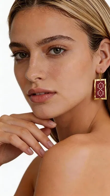, Τα statement κεντητά σκουλαρίκια με γεωμετρικά σχέδια σε μπορντό χρώμα αποτελούν τον τέλειο συνδυασμό παραδοσιακής τέχνης και σύγχρονης αισθητικής. Κατασκευασμένα από χρυσοκλωστή υψηλής ποιότητας, αυτά τα εντυπωσιακά σκουλαρίκια έχουν σχεδιαστεί από την Ελληνίδα Σχεδιάστρια Κοσμημάτων Αικατερίνη Χαλκιαδάκη, αποτυπώνοντας την αυθεντική ελληνική κοσμηματοτεχνία. Τα ορθογώνια κεντητά σκουλαρίκια διαθέτουν πολύπλοκα γεωμετρικά μοτίβα που δημιουργούν μια εκλεπτυσμένη vintage αισθητική. Το βαθύ μπορντό χρώμα συνδυάζεται αρμονικά με τις χρυσές λεπτομέρειες, δημιουργώντας ένα luxurious αποτέλεσμα που ταιριάζει τέλεια σε κάθε περίσταση. Η χειροποίητη κατασκευή εγγυάται την μοναδικότητα κάθε κομματιού, ενώ το ελαφρύ τους βάρος τα καθιστά ιδανικά για όλη την ημέρα. Αυτά τα boho σκουλαρίκια αποτελούν την τέλεια επιλογή για γάμους, ειδικές εκδηλώσεις ή για να προσθέσετε μια δόση κομψότητας στην καθημερινότητά σας. Υλικό: Ορείχαλκος, Ύφασμα Φροντίστε τα σκουλαρίκιά σας αποφεύγοντας την επαφή με νερό και αρώματα. Φυλάσσετε τα σε στεγνό μέρος για να διατηρήσετε τη λάμψη τους.
