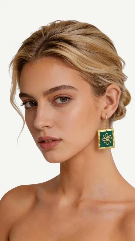 Τα εντυπωσιακά κεντητά σκουλαρίκια statement σε πράσινο χρώμα προσφέρουν μια μοναδική αισθητική που συνδυάζει την παραδοσιακή τέχνη του κεντήματος με σύγχρονο γεωμετρικό σχεδιασμό. Κάθε κομμάτι, σχεδιασμένο από την Ελληνίδα Σχεδιάστρια Κοσμημάτων Αικατερίνη Χαλκιαδάκη, αποτελεί έργο τέχνης που μετατρέπει κάθε εμφάνιση σε ξεχωριστή. Η χρυσοκλωστή που χρησιμοποιείται δημιουργεί εκθαμβωτικές αντανακλάσεις φωτός, ενώ το έντονο πράσινο χρώμα προσθέτει φρεσκάδα και ζωντάνια. Τα τετράγωνα κεντητά στοιχεία με το κεντρικό γεωμετρικό μοτίβο σε χρυσές αποχρώσεις δημιουργούν μια εκλεπτυσμένη αντίθεση που τραβά τα βλέμματα. Ιδανικά για ιδιαίτερες στιγμές και εκδηλώσεις, αυτά τα χειροποίητα σκουλαρίκια συμπληρώνουν τέλεια τόσο κλασικά όσο και μοντέρνα σύνολα. Η άνετη εφαρμογή και το ελαφρύ βάρος τα καθιστούν κατάλληλα για όλη τη μέρα. Υλικό: Ορείχαλκος, Ύφασμα Για τη διατήρηση της ομορφιάς τους, φυλάξτε τα σε στεγνό μέρος μακριά από άμεσο ήλιο.