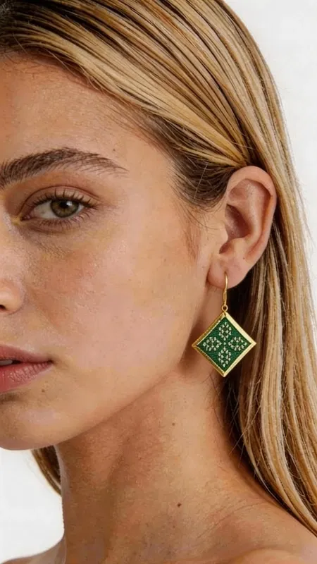 , Εντυπωσιακά κεντητά σκουλαρίκια statement που συνδυάζουν την παραδοσιακή τέχνη του κεντήματος με σύγχρονο γεωμετρικό design. Σχεδιασμένα από την Ελληνίδα Σχεδιάστρια Κοσμημάτων Αικατερίνη Χαλκιαδάκη, αυτά τα μοναδικά χειροποίητα σκουλαρίκια σε πράσινο χρώμα θα γίνουν το κεντρικό σημείο κάθε σας εμφάνισης. Το εκλεπτυσμένο ρομβοειδές σχήμα με τα λεπτομερή κεντητά μοτίβα από χρυσοκλωστή δημιουργεί μια κομψή αντίθεση με το έντονο πράσινο χρώμα. Κάθε σκουλαρίκι είναι χειροποίητο με ιδιαίτερη προσοχή στη λεπτομέρεια, συνδυάζοντας folklore design elements με μοντέρνα αισθητική. Ιδανικά για γάμο, ειδικές εκδηλώσεις ή όταν θέλετε να προσθέσετε μια δόση χρώματος και κομψότητας στην καθημερινότητά σας. Το ελαφρύ τους βάρος τα καθιστά άνετα για ολοήμερη χρήση. Συντηρήστε τα σκουλαρίκια σε στεγνό χώρο, αποφεύγοντας την επαφή με νερό και χημικά προϊόντα για να διατηρήσουν τη λάμψη και την ομορφιά τους.